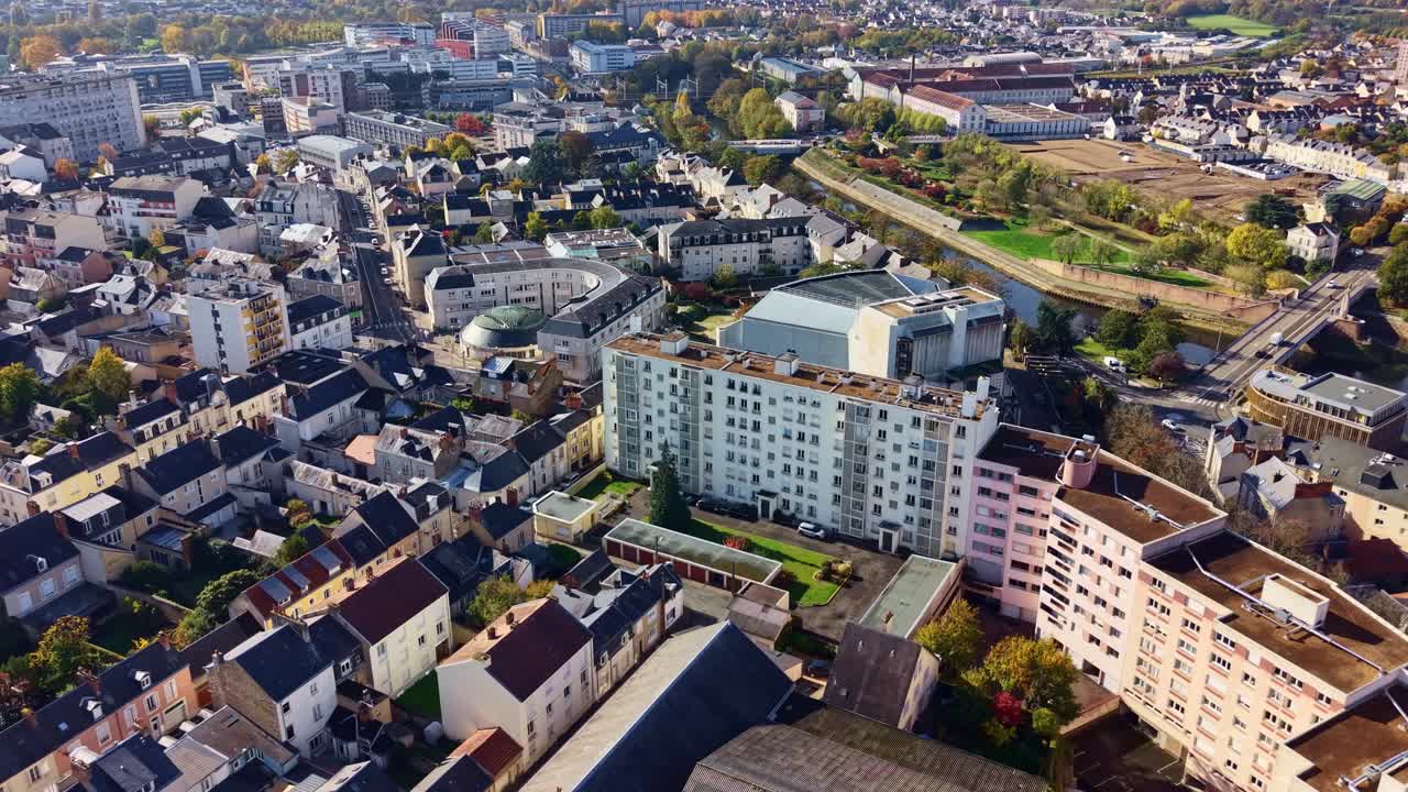 Forward drone shot over Le Mans city showing the Palais des Congrès, the Iron Bridge, and autumn-colored trees under a clear sunny sky