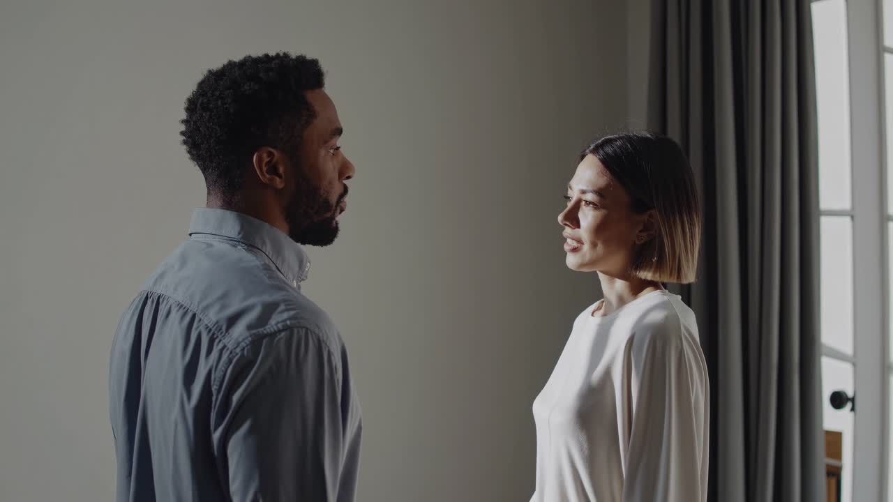 Man and a woman are standing in profile, engaged in a serious conversation in a naturally lit room, creating a calm and intimate atmosphere
