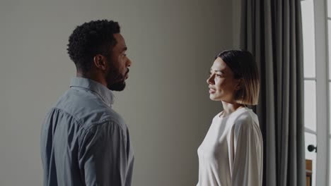 man and a woman are standing in profile, engaged in a serious conversation in a naturally lit room, creating a calm and intimate atmosphere