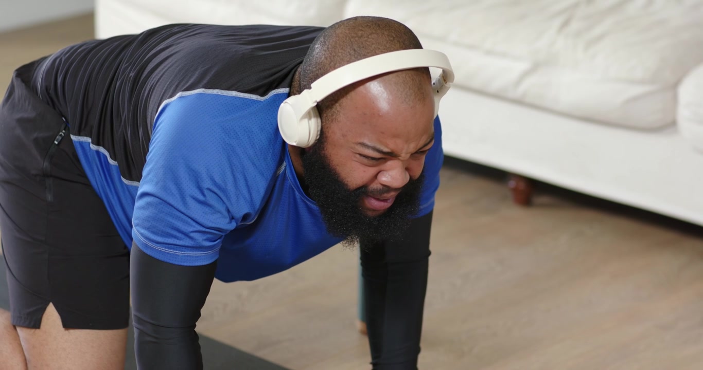 Placing hands on mat at home, African man moving into plank, donning headphones, holding for core