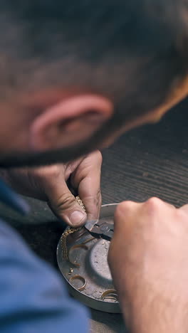 cu: goldsmith cuts leftovers from beautiful gold chain with pliers over box with wedding rings at workplace close back view