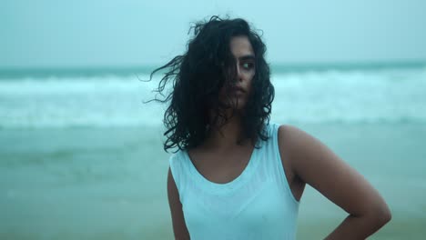 woman standing confidently on a beach with windswept hair and a serious expression, overcast day, close-up