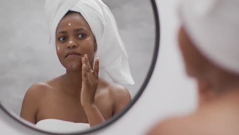 happy african american woman apply cream on face in bathroom