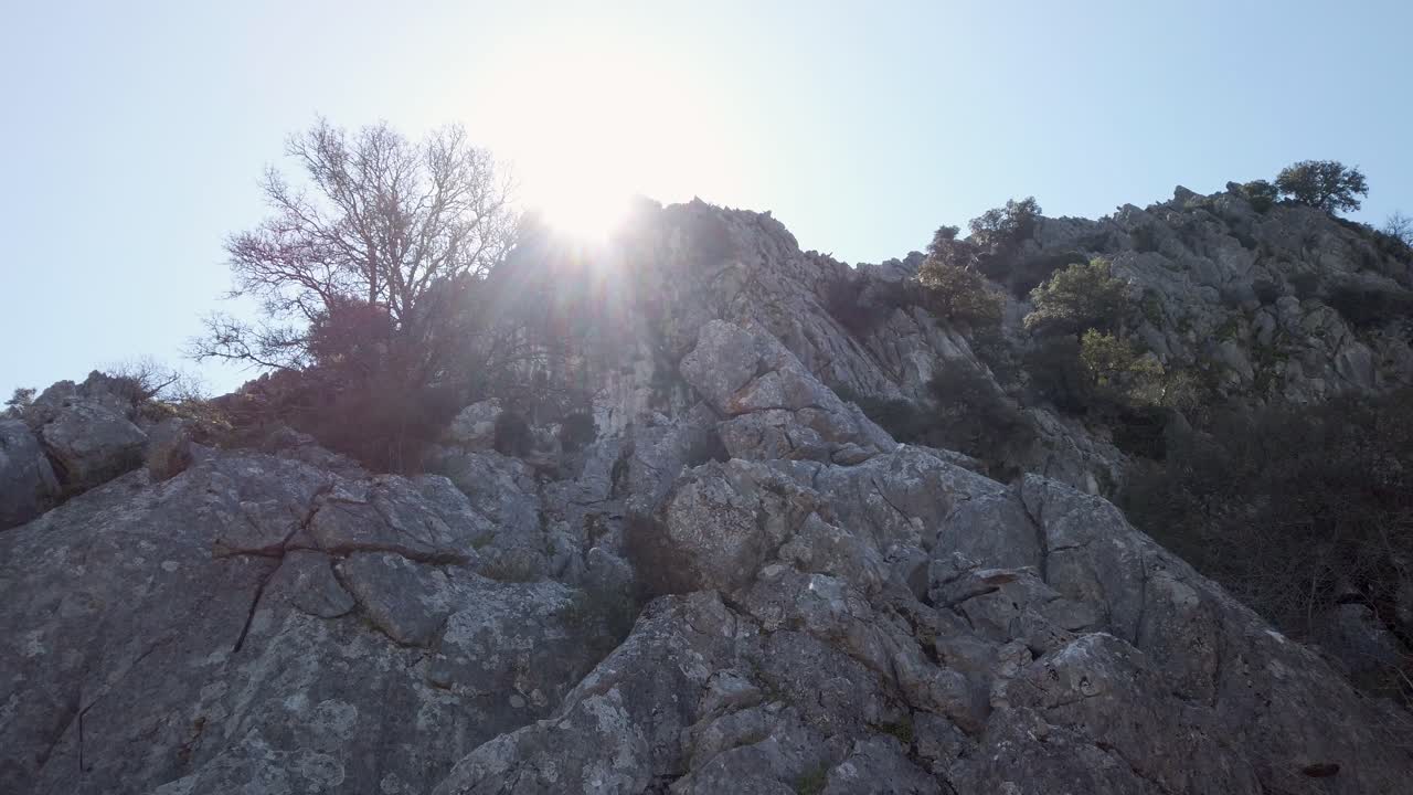 산의 바위 절벽 위에 빛나는 태양 플레어, 낮은 각도 공개
