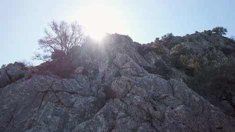 sun flare shining above rocky cliff face in mountains, low angle reveal