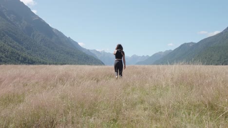 woman walks through a vast grassy field with mountains in the distance