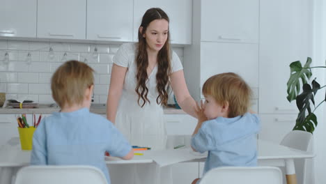 Mom-in-the-kitchen-washing-dishes-and-two-sons-sitting-at-a-Desk-drawing-on-paper-with-colored-pencils.