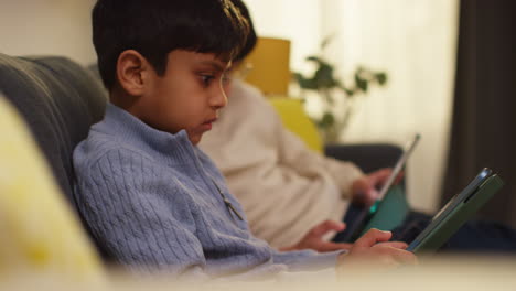 two young boys sitting on sofa at home playing games or streaming onto digital tablets 20