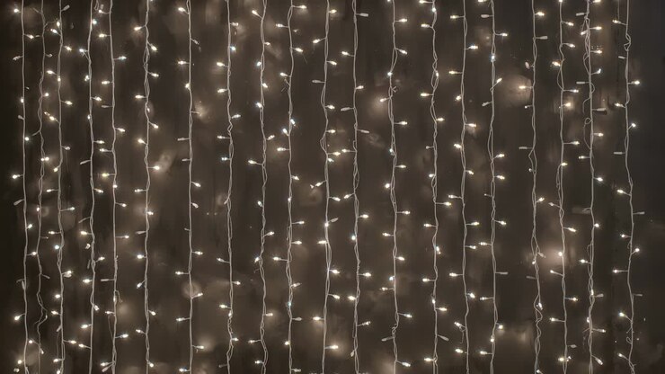 Shifting bulb brightness, warm white string light curtain flickering on dark wall, wires visible