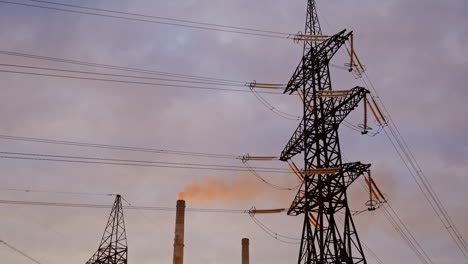 electricity pylon on industrial chimney background. high-voltage tower and pipe of power plant with smoke on evening sky. harmful smoke polluting the environment.