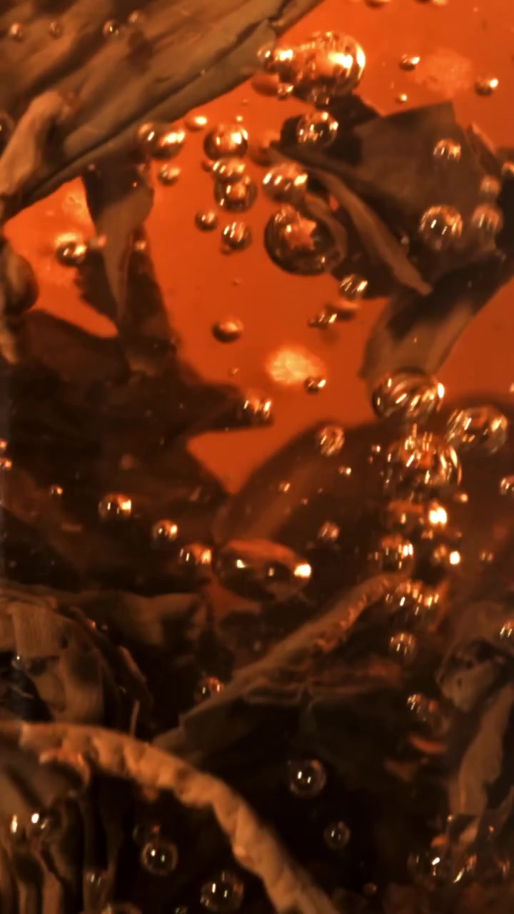 Primo piano di foglie di tè in infusione in acqua calda con bollicine.
