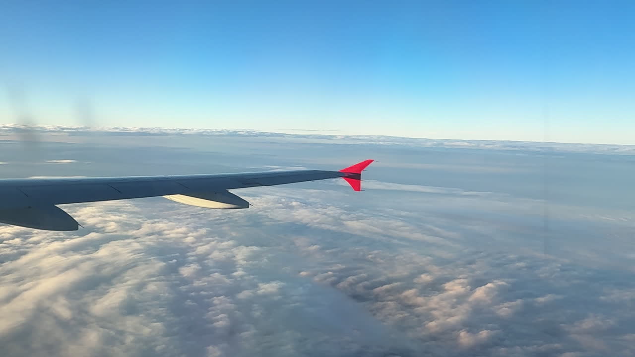 Vue depuis la fenêtre d'un avion montrant l'aile au-dessus d'une épaisse couche de nuages pendant le vol. Une lumière douce illumine les nuages et l'horizon, créant une scène aérienne paisible