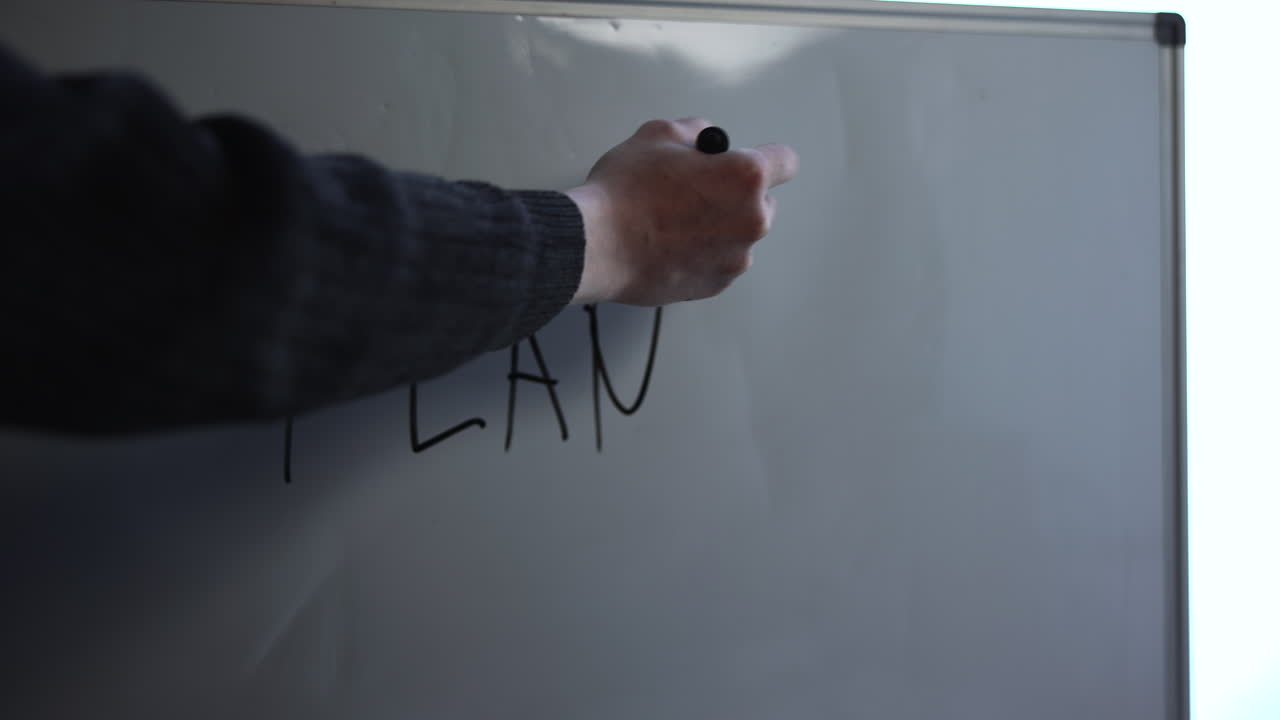 Escribiendo plan en pizarra con marcador, trazos de letras audaces forman la palabra "Plan", sesión de lluvia de ideas en la oficina.