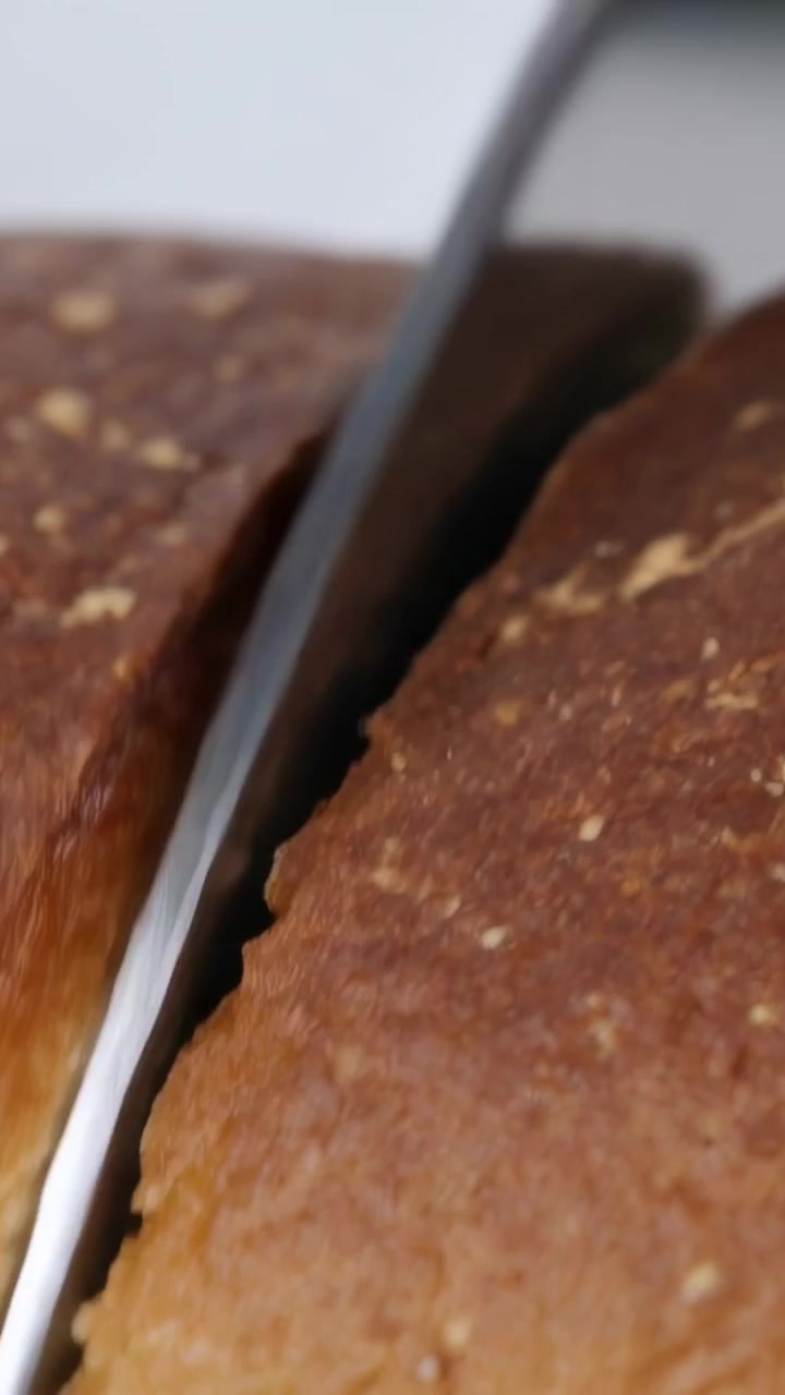 Video verticale: Coltello affilato che tocca la crosta, tagliando una pagnotta marrone in cucina, rivelando la mollica.
