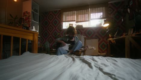 young woman playing guitar in a cozy bedroom