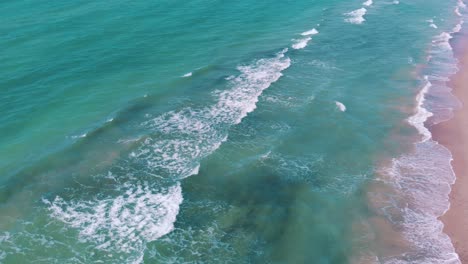 High-drone-aerial-shot-over-waves-breaking-on-a-pink-sand-beach-moving-out-to-sea