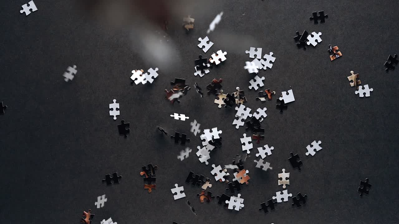 직소 퍼즐 조각들이 슬로우 모션으로 회색 테이블 위로 아래로 떨어지고 초점이 맞지 않는 얕은 피사계 심도 확대