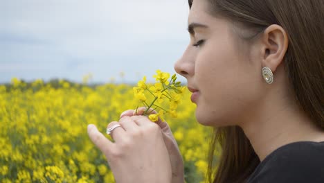 Brown-haired-girl-smelling-yellow-flowers-of-rapeseed-under-the-dark-gray-sky
