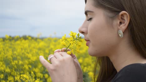 brown haired girl smelling yellow flowers of rapeseed under the dark gray sky