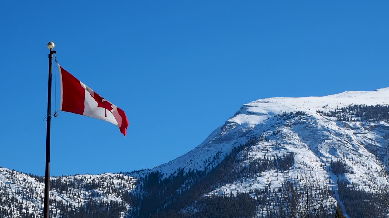 Kanadische Flagge weht im Wind mit schneebedeckten Bergen im Hintergrund