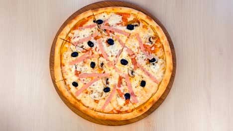 slicing pizza with ham and cheese on wooden board on the table. close-up view.