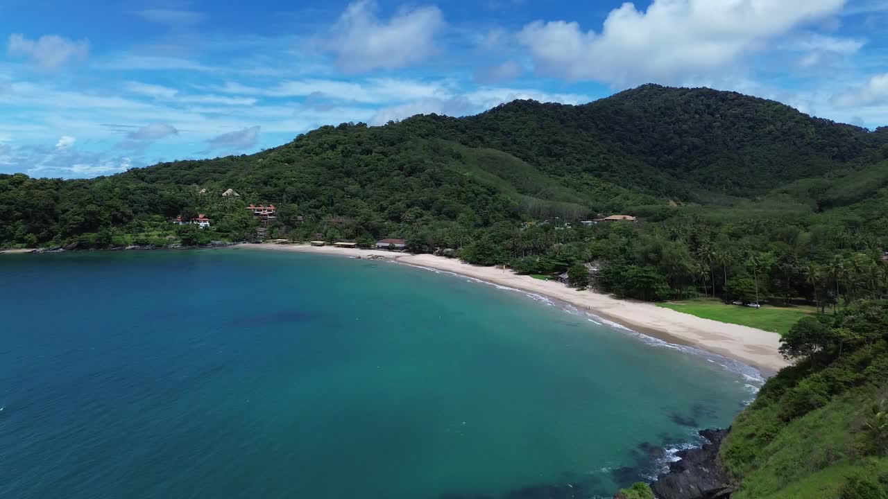Aerial drone view of a remote Koh Lanta beach with lush green hills, dense forest and a few scattered coastal bungalows, showing turquoise water and peaceful tropical island scenery without crowds