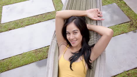 a young biracial woman relaxes on a poolside lounger in her backyard at home