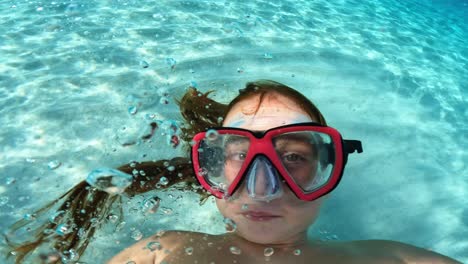 podwodne selfie młodej rudej dziewczyny z maską do nurkowania trzymającej aparat podczas zabawy w krystalicznie turkusowej wodzie morskiej