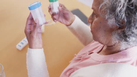 Senior-african-american-woman-sitting-at-table,-taking-pills