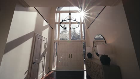 a large entry way to a luxury home with a modern chandelier and sun flares leaking through large windows