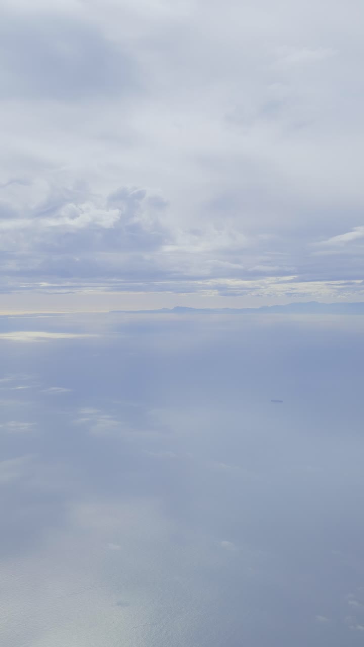 Soft, aerial view of calm, vast ocean and cloudy sky from an airplane window