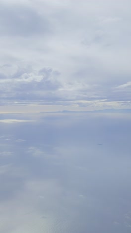 soft, aerial view of calm, vast ocean and cloudy sky from an airplane window