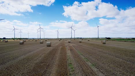A-breathtaking-aerial-video-captures-the-graceful-dance-of-wind-turbines-in-a-Lincolnshire-farmer's-newly-harvested-field,-with-the-added-charm-of-golden-hay-bales
