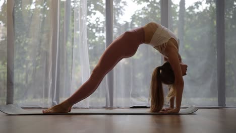 woman practicing yoga bridge pose near a window