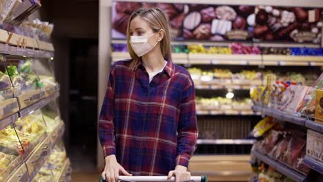 young woman carries a cart in the supermarket during the quarantine period in mask