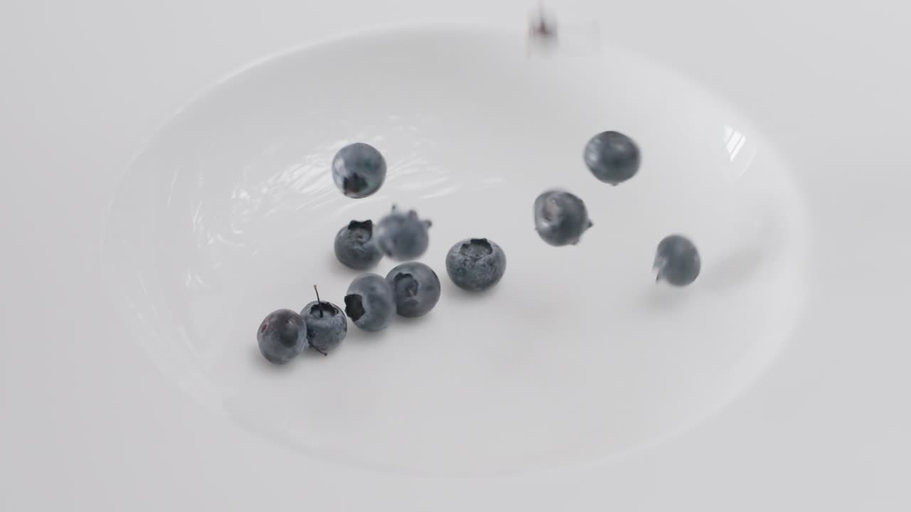 Close-up slow motion of fresh organic blueberries falling into a clean white bowl, food and health concept