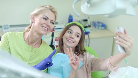 médico sorridente e paciente tirando uma selfie no consultório do dentista. mulher mostrando sinal de v