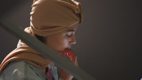 Asian-female-student-wearing-a-beige-hijab-sitting-on-stairs-and-using-a-laptop