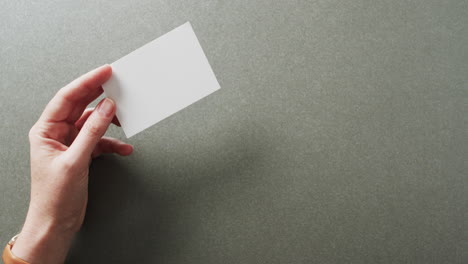 hand of caucasian woman holding white business card on grey background, copy space, slow motion