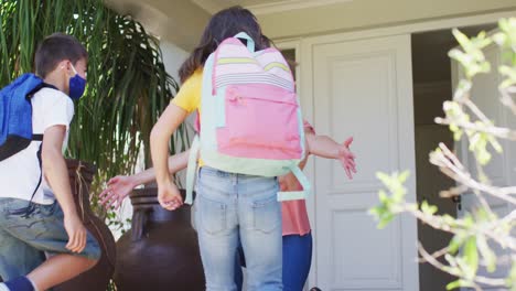 Caucasian-boy-and-girl-wearing-face-mask-hugging-their-mother-after-coming-from-school