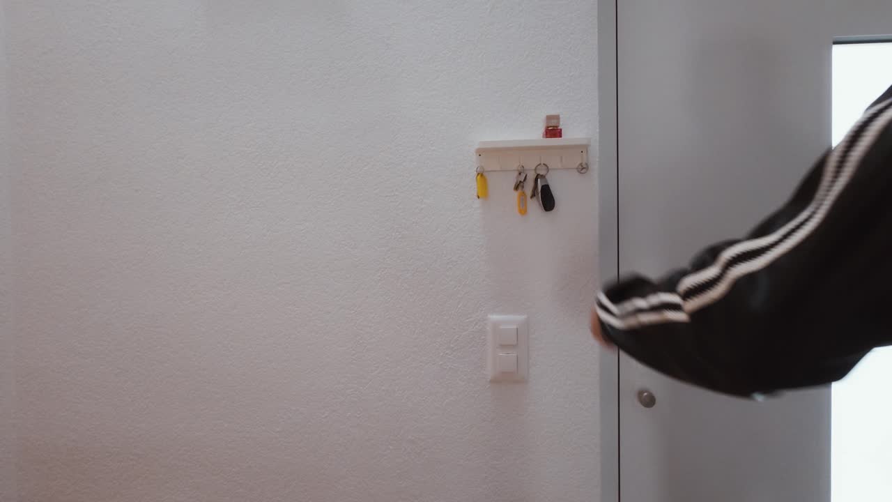 A man hangs his key on a wall-mounted hook next to the entrance door. Simple everyday moment symbolizing home organization, routine, minimalism, and daily life habits