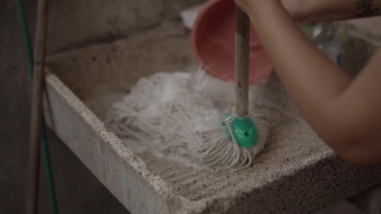 Close up of person cleaning concrete basin with mop in outdoor area, showing wet surface, textured stone construction and manual household cleaning activity