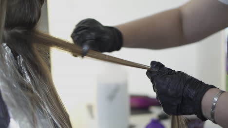 a close-up view of a hairdresser in black gloves preparing a client’s hair for balayage coloring.