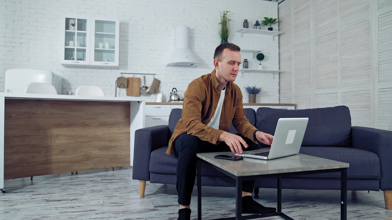 Young male working from home. Portrait of freelancer man working on laptop at home sitting on couch. Quarantine remote work.