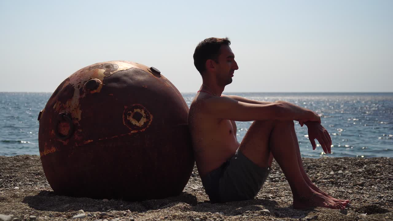hombre haciendo ejercicio de yoga al aire libre cerca de una vieja mina marina flotante oxidada en la playa con costa rocosa y fondo marino. estilo de vida saludable, contaminación, protección de la naturaleza, concepto de guerra y paz