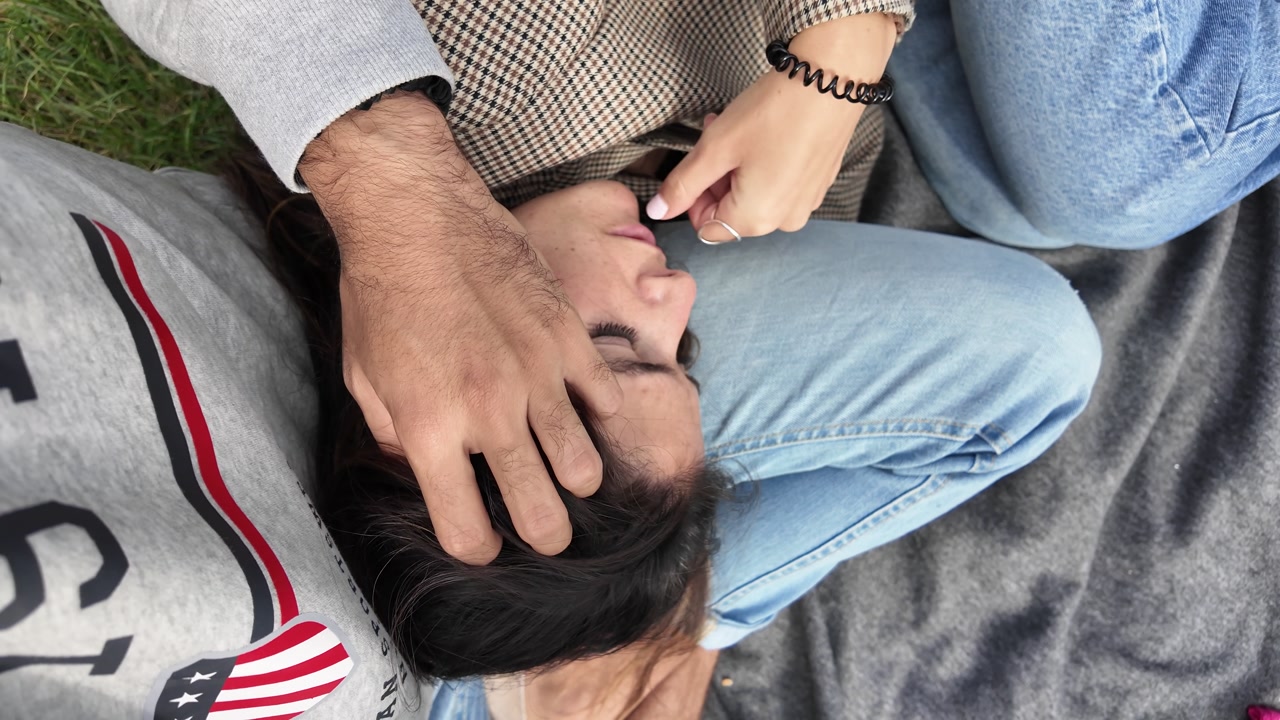Young man caressing his girlfriend’s head as she rests on his lap outdoors, slow motion