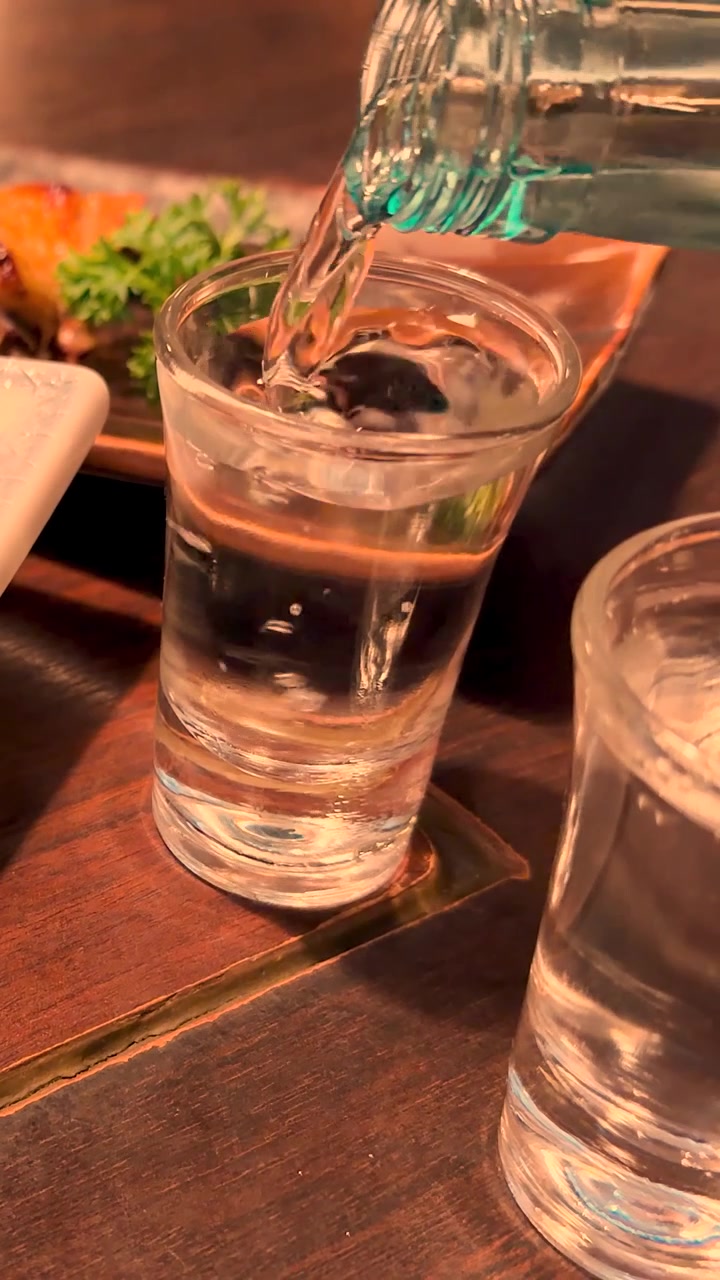 Primo piano di sake giapponese trasparente versato da una bottiglia in un bicchiere a Tokyo.