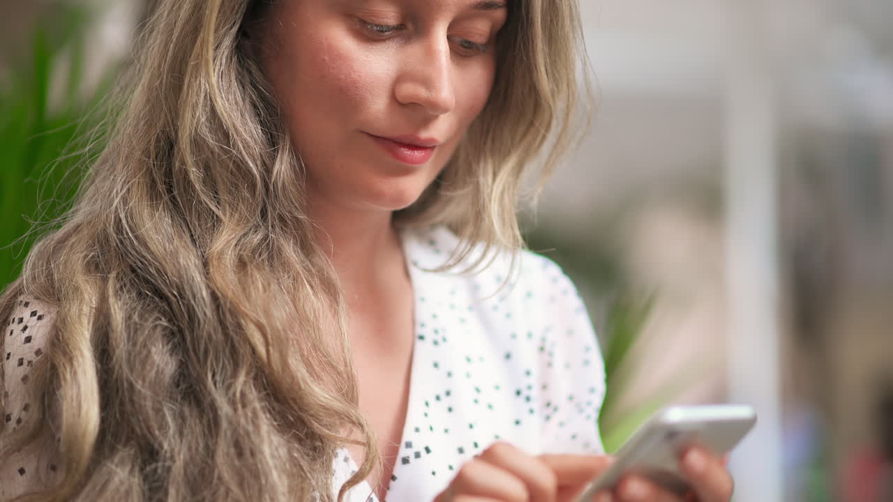 Caucasian blonde woman in a dress is using her smartphone outdoors