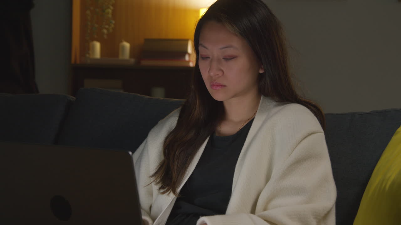 여성은 집에서 저녁을 보내고 소파에 앉아 노트북 컴퓨터로 소셜 미디어 스트리밍을보고 온라인 스크롤을합니다.