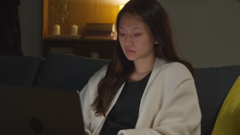 여성은 집에서 저녁을 보내고 소파에 앉아 노트북 컴퓨터로 소셜 미디어 스트리밍을보고 온라인 스크롤을합니다.